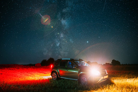 Night Starry Sky With Glowing Stars Above Car SUV In Countryside Landscape. Milky Way Galaxy And...