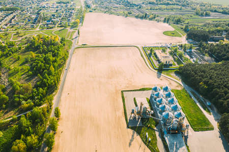 Aerial View Modern Granary, Grain-drying Complex, Commercial Grain Or Seed Silos In Sunny Spring Rural Landscape. Corn Dryer Silos, Inland Grain Terminal, Grain Elevators Standing In A Fieldの写真素材