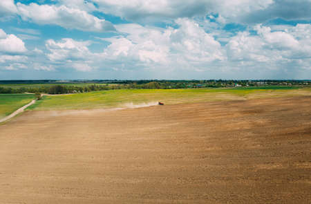 Red Tractor Plowing Field In Spring Season. Beginning Of Agricultural Spring Season. Cultivator Pulled By A Tractor In Countryside Field. Aerial View Rural Field Landscapeの写真素材
