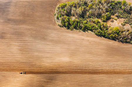 Tractor Plowing Field In Spring. Beginning Of Agricultural Season. Cultivator Pulled By A Tractor In Countryside Rural Field. Countryside Field Landscape. Aerial View. Top Flat Viewの写真素材