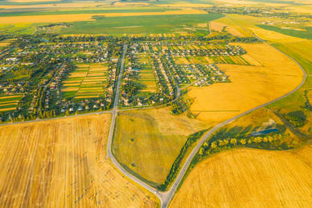 Aerial View Of Village And Hay Rolls, Straw Field Landscape In Summer Evening. Haystack, Hay Roll in Sunrise Time. Agricultural Countryside landscape In Harvest Season.の写真素材
