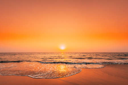 Sunset Sun Above Sea. Natural Sunrise Sky Warm Colors Over Ripple Sea. Ocean Water Foam Washing Sandy Beach At Sunsetの写真素材