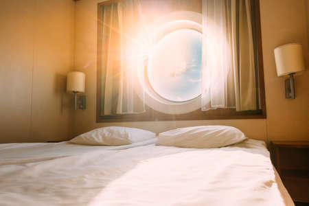 Natural Sunlight Shining Through Ship Window In Craft Cabin With Bed. View On Sea. Luxury Cabin On Ferry Boat Or Cruise Liner. Sea Cruise Vacation Trip Travel Conceptの写真素材