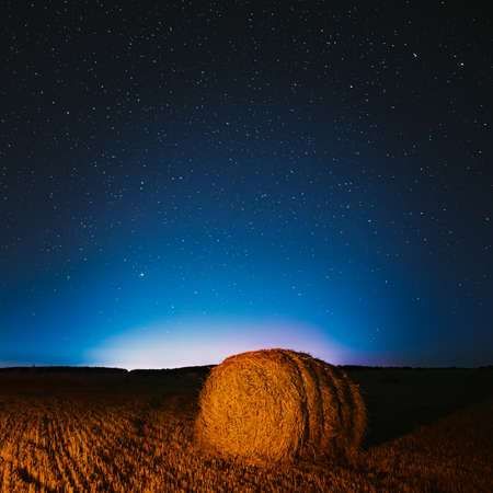 Night Starry Sky Above Haystacks In Summer Agricultural Field. Night Stars Above Rural Landscape With Hay Bales After Harvest. Agricultural Conceptの写真素材