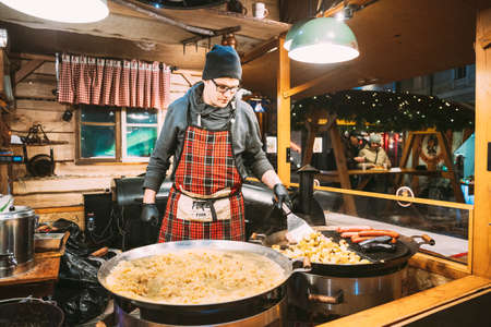 Tallinn, Estonia. Man frying potatoes and sausages - a traditional Christmas dish of street food on streets of Europe in winter during the Christmas holidays.のeditorial素材