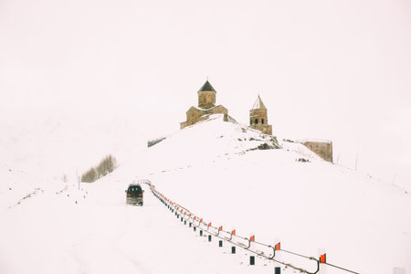 Stepantsminda, Gergeti, Georgia. Car Goes To Famous Ancient Gergeti Trinity Tsminda Sameba Church In...