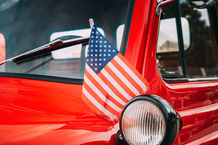 Red Pickup Truck With Small American Flag Waving. Close Side View Of Red Pickup Truck American Flag Waving. 4th of July holiday. American flag blowing in the wind. Independence Dayの写真素材