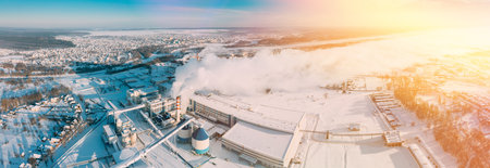 panorama Factory Bird's-eye View At Sunny Snowy Winter Day. Plant Pipe With Escaping Steam Or Smoke. Aerial View Top Elevated View Winter Snowy Forest Landscape. Steam Light Clouds Flowing On Air. Sunny Winter Frozen Day. Misty Morning Sunrise.の写真素材