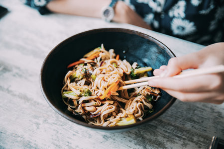 Woman eating asian noodles udon with pork in cafe. Asian noodles udon with pork close-up in a bowl on the tableの写真素材