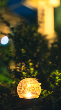 Amazing Small Garden With Yellow Light, Lamp In Flower Bed. Garden Design. Solar Powered Lamp At Summer Night Garden. Ecological Energy Concept. Magic Yellow Light. Ecofriendly Energy Lightの写真素材
