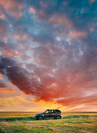 AWD 4WD SUV green car in summer meadow landscape in summer field countryside landscape. Sunset sky backgroundの写真素材