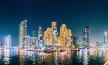 Dubai Marina Port, UAE, United Arab Emirates - May 19, 2021: Beautiful Night view of high-rise buildings of residential district in Dubai Marina And Tourist Boat, Sightseeing Boat Sailing On Dubai Marina. Panorama, Panoramic Viewのeditorial素材
