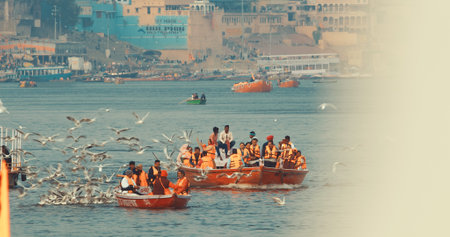 Varanasi, India. Tourists And Indian Pilgrims Floating On Ganga Riverbank. Tourists Boats Floating And Feeding Seagulls On Ganges River. Many Gulls Birds Flying Follow Boats. Boat Ride On Ganges Riverのeditorial素材