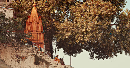 Varanasi, India. Tourists And Indian Pilgrims Sitting On Steps Of Ganges Embankment, Shivala Ghat. Shree Ganesha Temple Background. Every Day Life Of India. Morning At Sacred Hanuman Ghatのeditorial素材