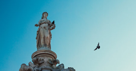 Mumbai, India. Pigeon Sits On Flora Fountain. Fly Of Pigeons Above Flora Fountain. Fountain Located At Hutatma Chowk Is Ornamentally Sculpted Architectural Heritage Monument. Located At Southern End Of Historic Dadabhai Naoroji Road. Roman Goddess Flora. Clear Blue Skyの写真素材
