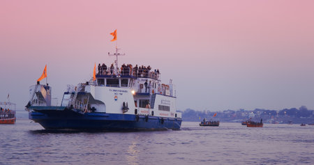 Varanasi, Uttar Pradesh, India. Tour boat ship floating on Ganga river. Purple sunset sky at evening time. Camera moving along riverbank embankment.のeditorial素材