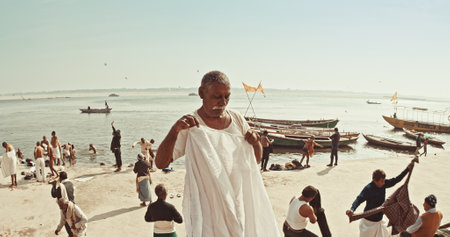 Varanasi, Uttar Pradesh, India. Man dry clothes after wash. Harishchandra ghat at morning. Indian men take their morning bath in sacred waters of the Ganges River. Pilgrims having a morning bath and pray. Boats moored at on the Ganges river embankmentのeditorial素材