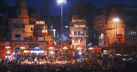 Varanasi, Uttar Pradesh, India. Many people visiting Ganga Maha Aarti ceremony on Dashashwamedh Ghat. night time illumination lights. Cinematic Camera movement moving along riverbank embankment. View from riverside. Skyline in night lights. People visitinのeditorial素材