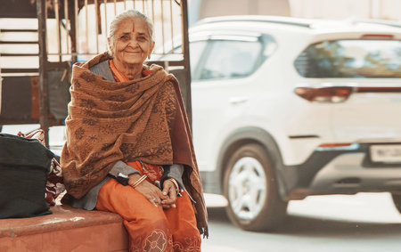 Jaipur, Rajasthan, India. Old Indian Woman in traditional dresses sari sitting in street and Looking At Camera And Smiling In Summer evening Sunlight.のeditorial素材
