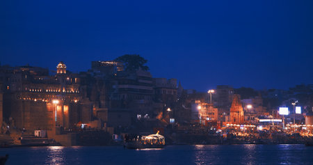 Varanasi, Uttar Pradesh, India. Boats floating near Rana Mahal Ghat, Darbhanga Ghat and Dashashwamedh Ghat in night time illumination lights. Cinematic Camera movement moving along riverbank embankment. View from riverside. Skyline in night lights. View from boat. Many Hindu templesの写真素材