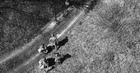 Historical Re-enactment Black And White . Men Dressed As US American Soldiers Of USA Infantry Of World War II sneaking around In spring Autumn Day. Soldiers prepare mortar for battle In dry grass. Aerial view elevated shotの写真素材