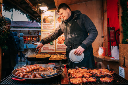 Tallinn, Estonia. Man frying potatoes and sausages - a traditional Christmas dish of street food on streets of Europe in winter during the Christmas holidays.のeditorial素材