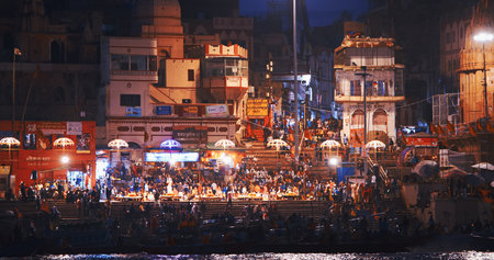 Varanasi, Uttar Pradesh, India. Many people visiting Ganga Maha Aarti ceremony on Dashashwamedh Ghat. night time illumination lights. Cinematic Camera movement moving along riverbank embankment. View from riverside. Skyline in night lights. People visitinのeditorial素材