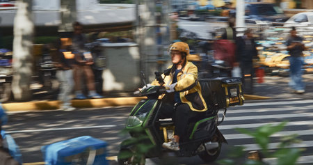 Delivery rider in yellow gear crossing the street amidst city hustle. Shanghai, Chinaのeditorial素材
