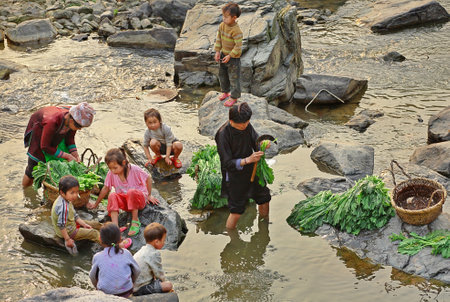 Zengchong village, Guizhou, China - April 11, 2010: The countryside of southwestern China, women with children, wash their herbs in rural river, Zengchong Dong ethnic minority village, April 11, 2010. Asian with children, washed greens in a rural river.のeditorial素材