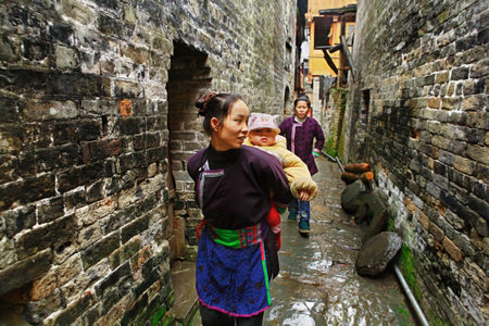 Zengchong village, Guizhou, China - April 13, 2010  Chinese woman walks along a narrow street Asian village, holding baby behind him, Zengchong Dong ethnic minority Village, Guizhou, China - April 13, 2010のeditorial素材