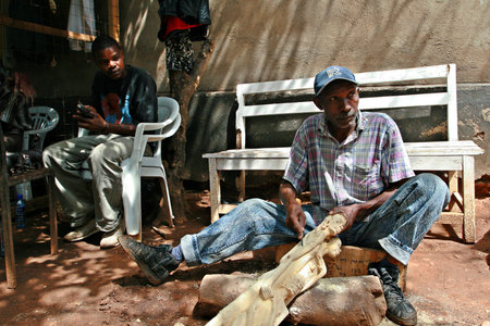 Namanga, Tanzania - February 9, 2008: African black wood-carver, working art workshop. Dark-skinned African man, the master woodcarving, carving wooden statues of Maasai women.のeditorial素材