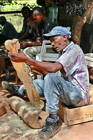 Namanga, Tanzania - February 9, 2008: Dark skinned middle-aged African, master wood carving works of art workshop, under the open sky. Art workshop outdoors woodcarver carves Maasai figurines. Editorial Use Onlyのeditorial素材