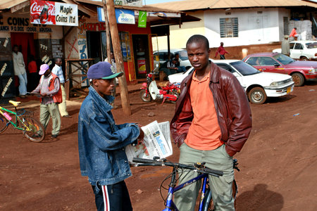 Makuyuni, Arusha, Tanzania - February 13, 2008: Young black African men met on the village street, one holding a newspaper Mwananchi, with text in Swahili, the other sits on the old bike.のeditorial素材