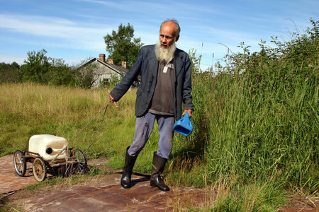 Leningrad area of St. Petersburg, Russia - July 22, 2006: Valentin Stepanovich Shramko born in 1938, Elderly, graybeard man peasant farmer pulls a cart with the canister well water.のeditorial素材