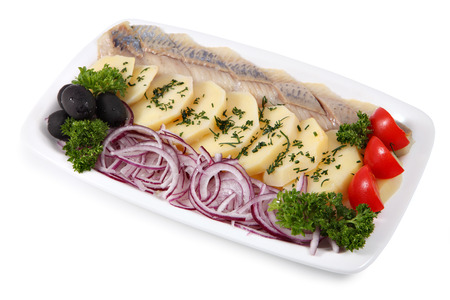 White oval plate with slices of pickled herring fillets, fresh onion rings, and boiled potatoes sprinkled with dill isolated on a white background.の写真素材