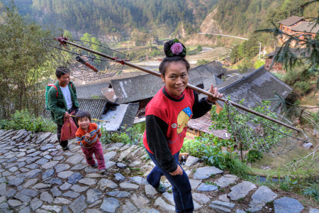 Langde Village, Guizhou, China - April 15, 2010: Woman farmer with a rose in her hair is on rural stoun road, Langde Miao Village.のeditorial素材