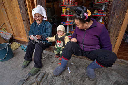 Langde Village, Guizhou, China - April 16, 2010: Two rural Chinese woman sitting on the threshold of the village shop, next to a year-old baby.のeditorial素材