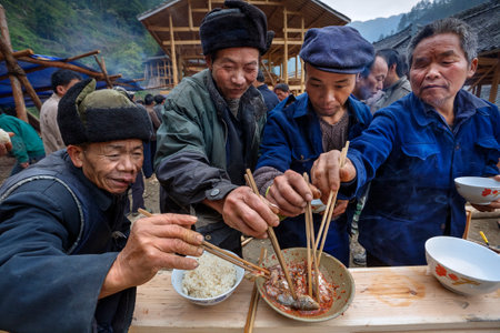 Langde Village, Guizhou, China - April 16, 2010: Festive ceremony of the start of construction of  new peasant farmhouse, guests rural holiday together eat fish and rice using chopsticks, Miao villageのeditorial素材