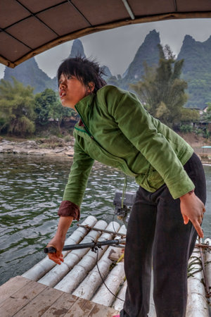 Yang Di village, Yangshuo, Guangxi, China - March 29, 2010: Chinese boatmen women Lijiang River, bamboo raft with an outboard motor, ferryman Asian girl in a green jacket, operates ferry.のeditorial素材
