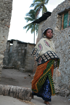 Zanzibar, Tanzania - February 20, 2008: Unknown barefoot dark-skinned African Muslim girl in head scarf, is on a narrow street fishing village.のeditorial素材