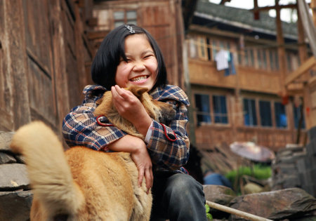 Guangxi, China -  April 3, 2010: Unknown Chinese girl about 8 years old, hugging light brown dog, village Dazhai, near Longsheng.のeditorial素材