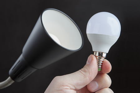 LED electric light bulb in human hand near the lampshade a floor lamp, against a dark background.の写真素材