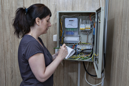Woman takes readings of electricity meters, standing near the electrical switchgear inside.の写真素材