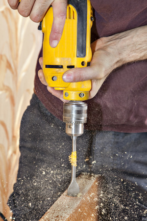 Door lock installing using  yellow electric drill, carpenter spade bit to drill through edge door for hole latch, wood sawdust flying around.の写真素材