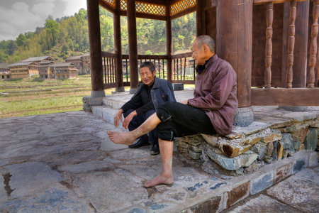 Zhaoxing Dong Village, Guizhou Province, China -  April 8, 2010: Two elderly Asian men resting in the shade under the roof of a covered bridge near the village of ethnic minorities.のeditorial素材