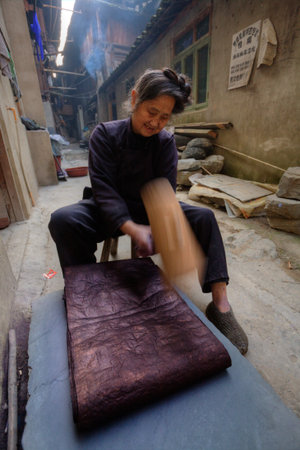 Zhaoxing Dong Village, Guizhou Province, China -  April 9, 2010: Dong woman pounding dyed cotton...