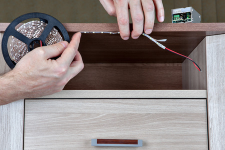 Using LED strip light lighting for indoor furniture, close-up human hands glued tape on board.の写真素材
