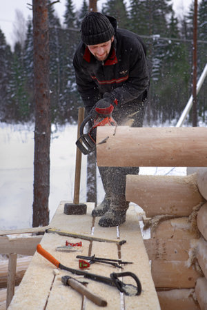 Leningrad Region, Russia - February 2, 2010: Construction of wooden log cabins makes the notch on the end of the log using a chainsaw.のeditorial素材
