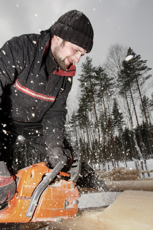 Leningrad Region, Russia - February 2, 2010: Construction worker trimming a log with a chainsaw, the sawdust flying.のeditorial素材