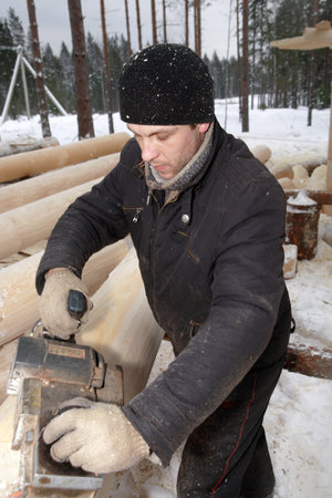 Leningrad Region, Russia - February 2, 2010: Carpenter sanding a log using an electric planer.